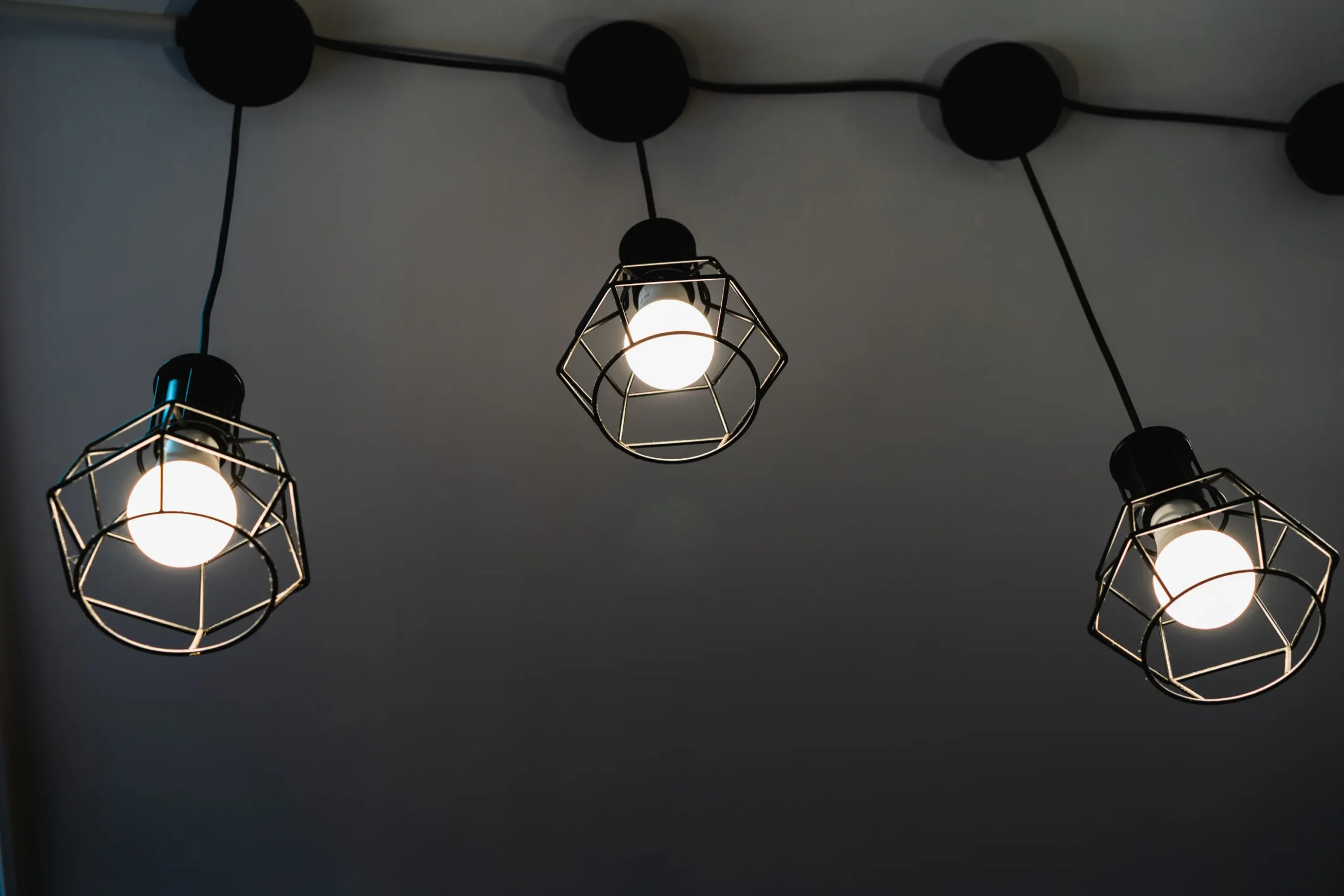 "Modern geometric pendant lights with wire cage design against dark ceiling"