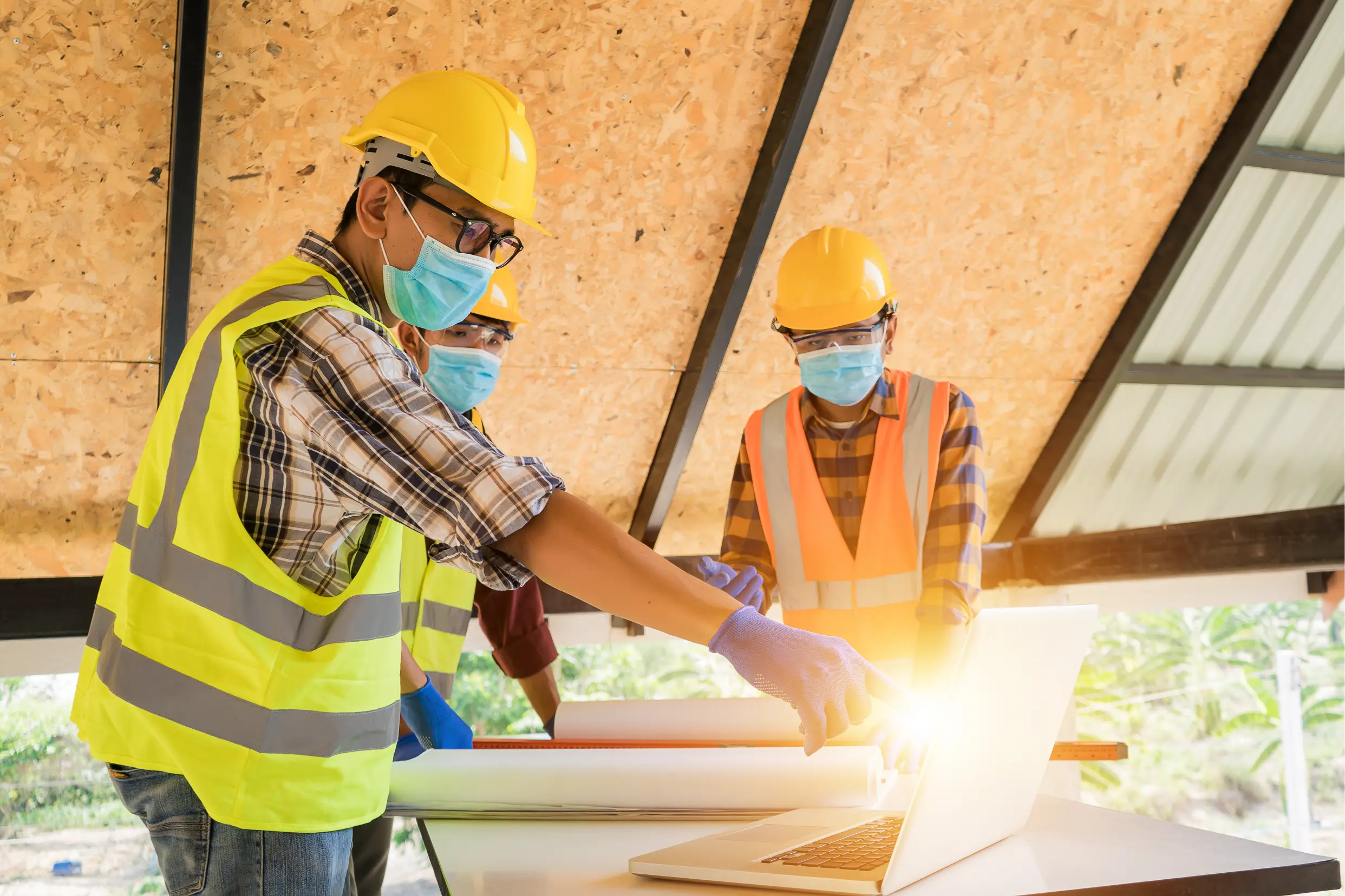 "Construction engineers reviewing blueprints wearing safety gear and masks during site meeting"