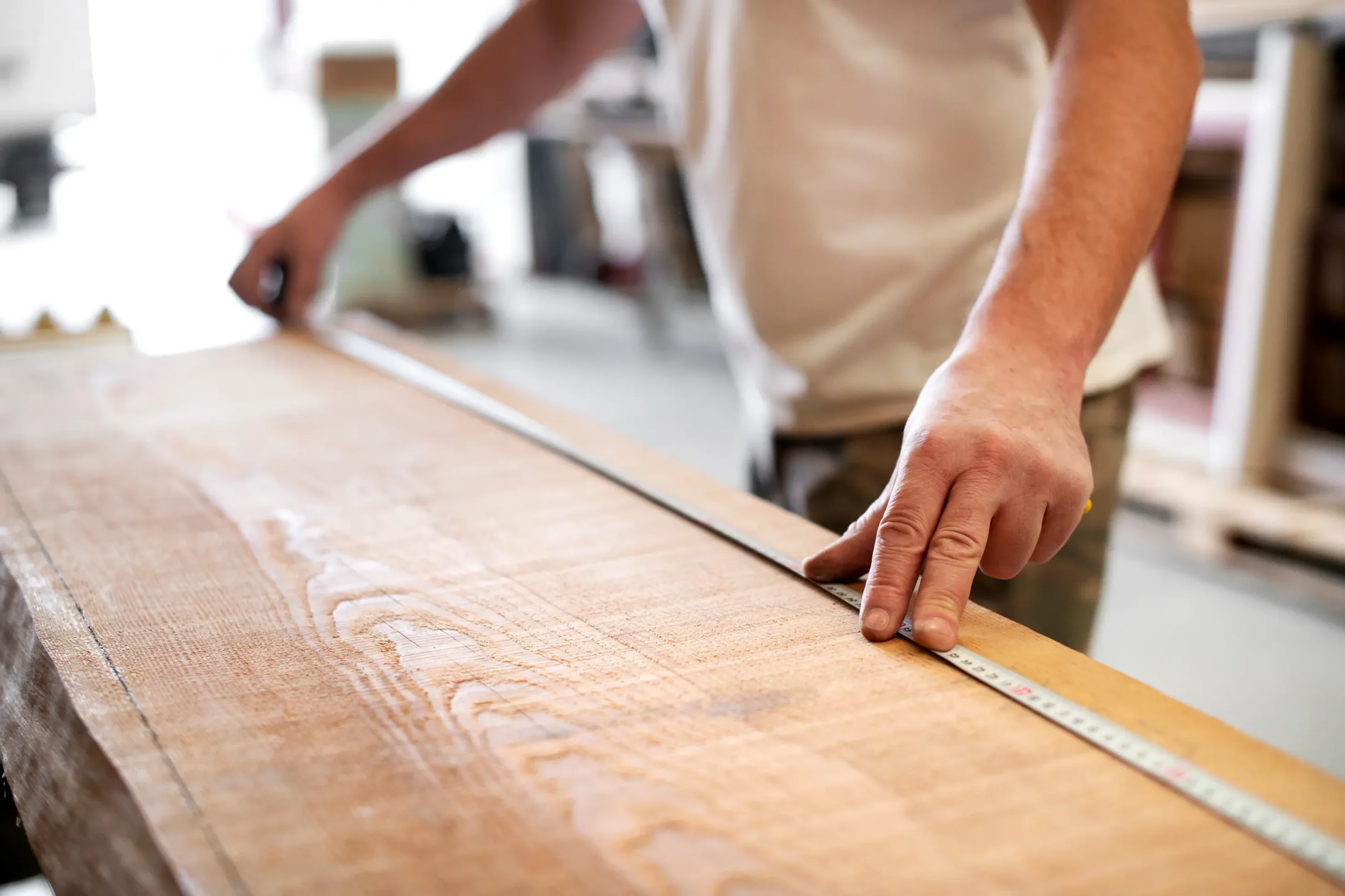 "Professional carpenter measuring wooden plank with measuring tape for precise woodworking"