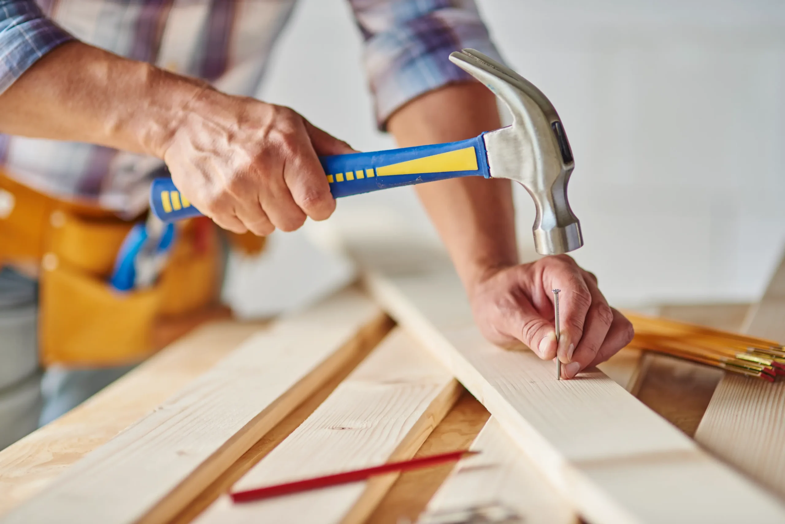 "Professional carpenter hammering nail into wooden plank during home renovation"