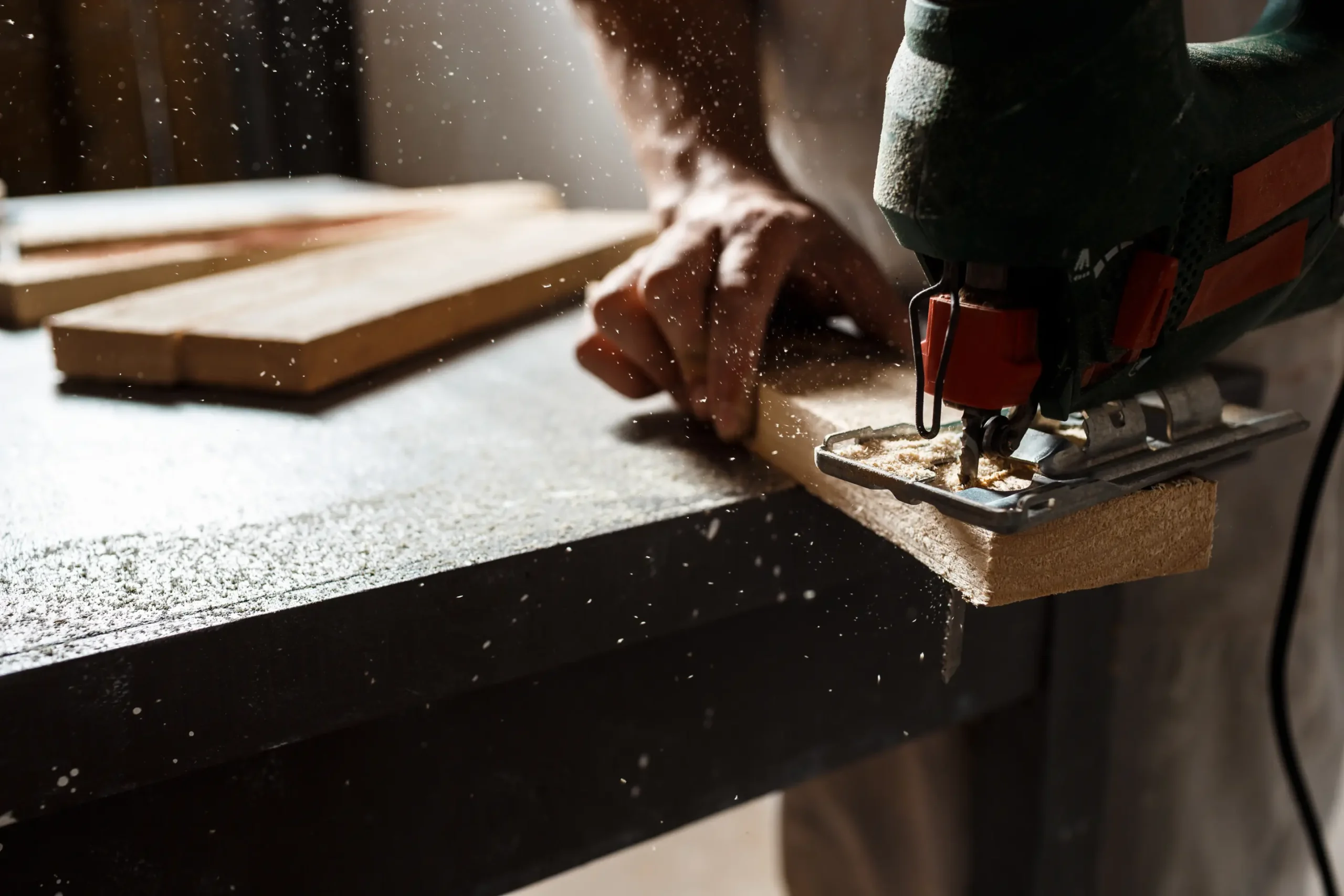 "Close-up of electric jigsaw cutting wooden board with sawdust particles floating in workshop"