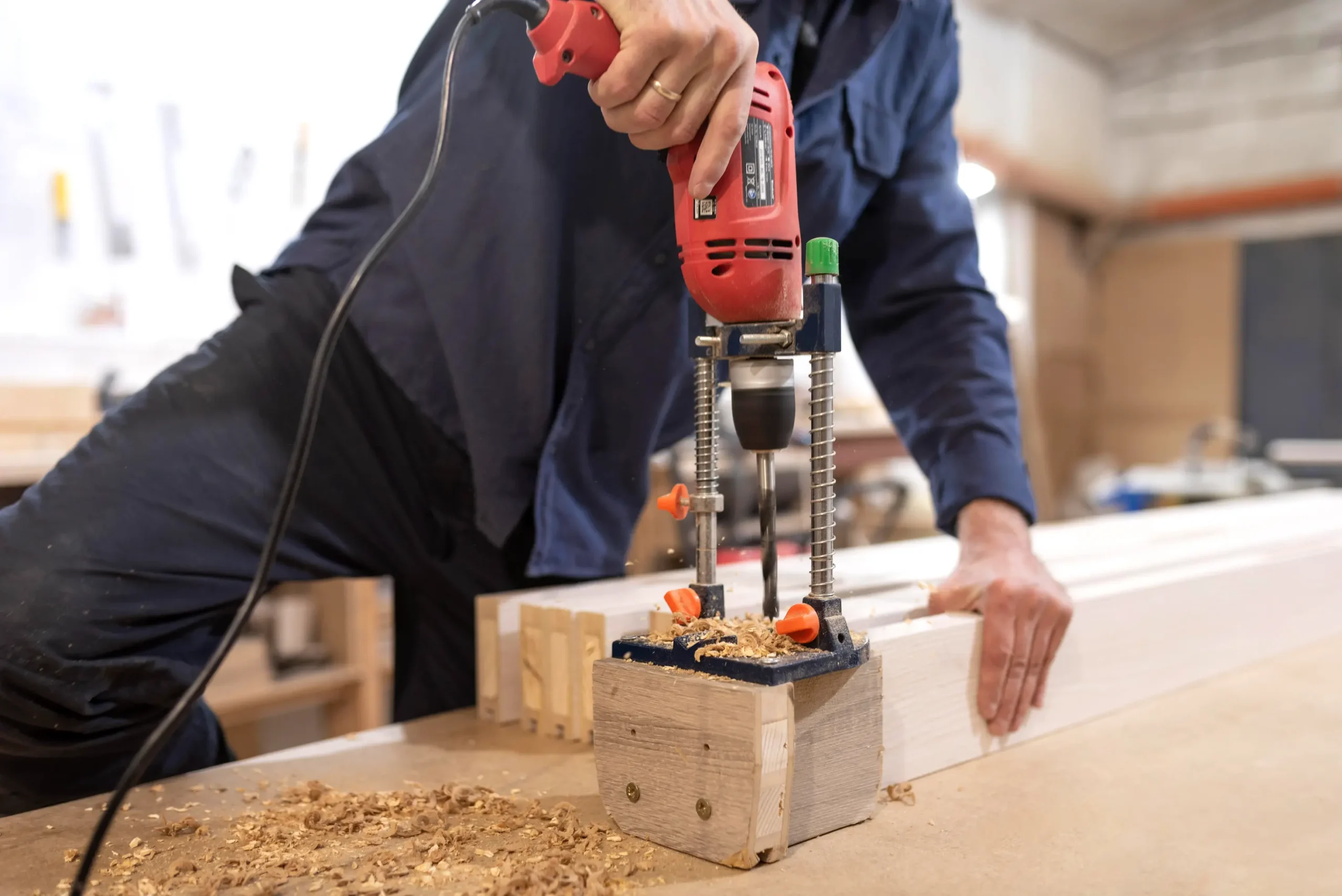 "Carpenter using drill press stand with guide rails for precise woodworking in professional workshop"