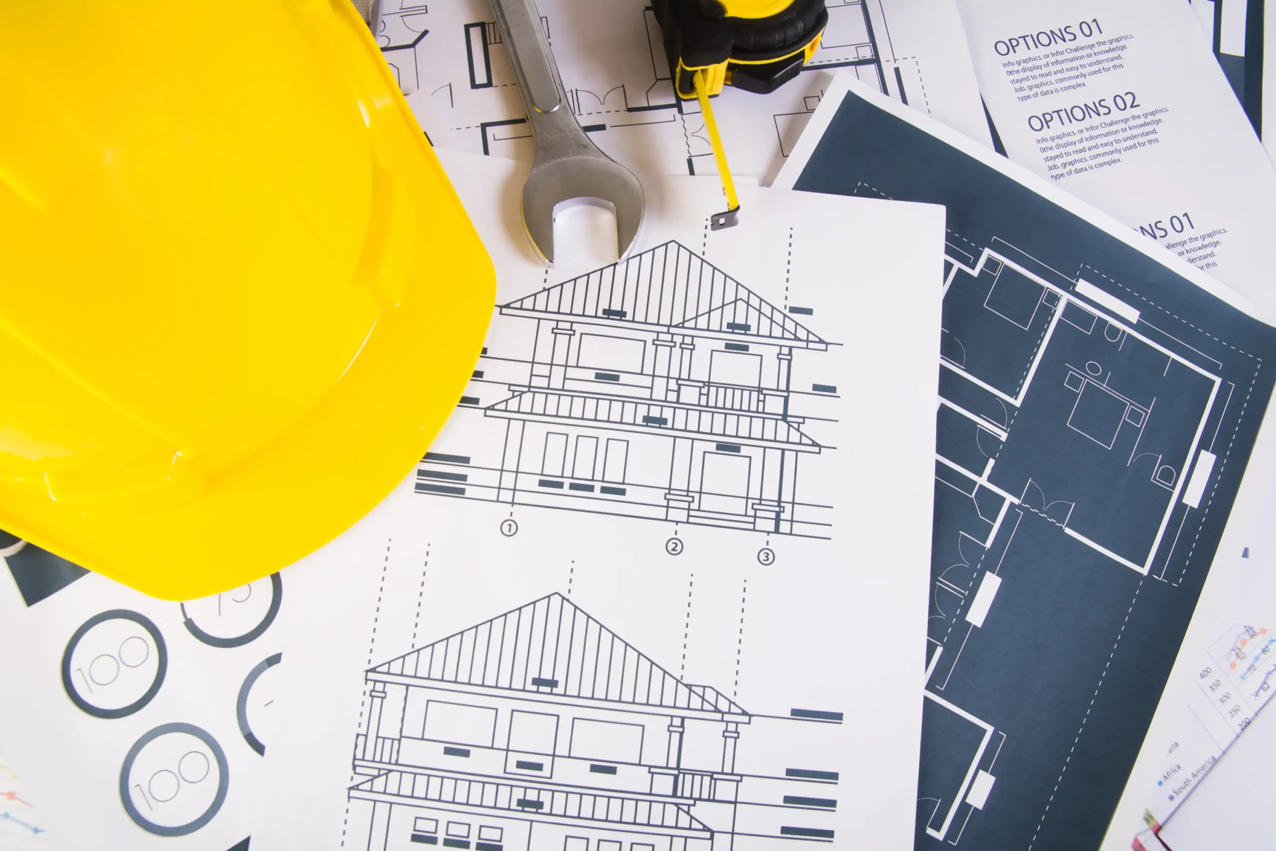 "Construction blueprints with yellow hard hat, wrench, and floor plans on architect's desk"