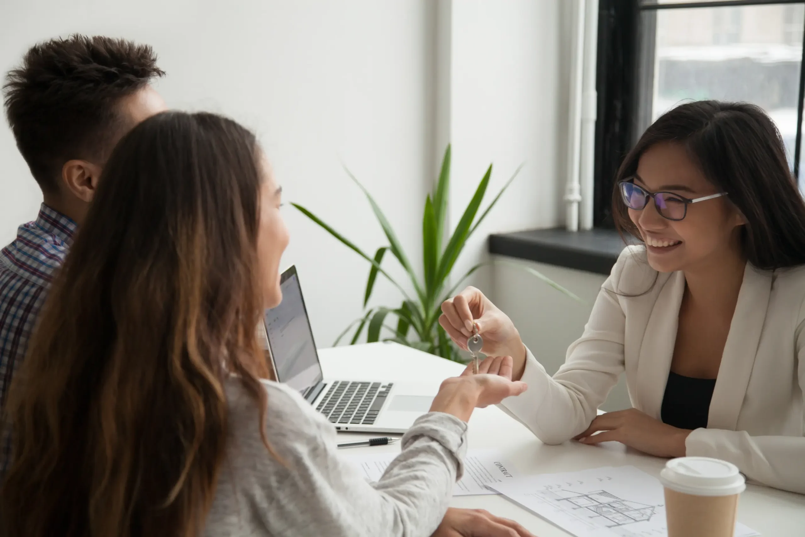 "Real estate agent handing house keys to young couple during property purchase meeting"