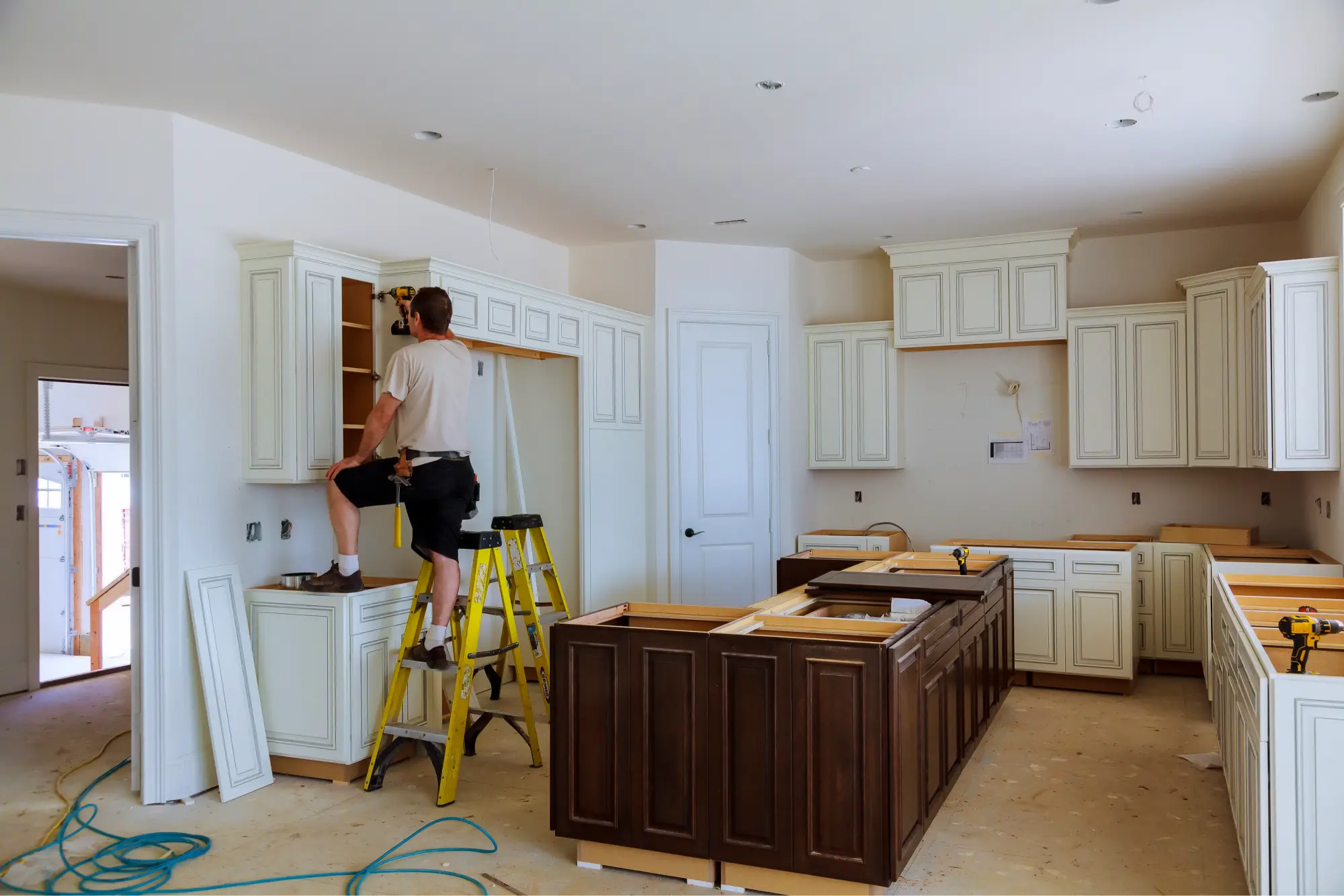 "Professional kitchen cabinet installation in progress with craftsman mounting white shaker-style cabinets and dark wood island"