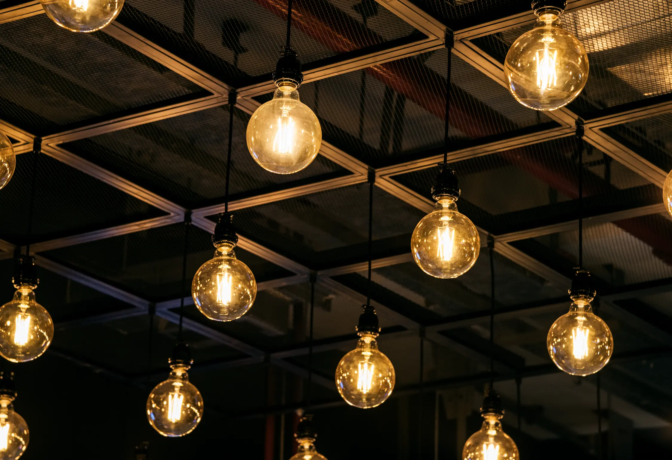 "Vintage Edison LED bulbs hanging from industrial ceiling with geometric grid pattern"