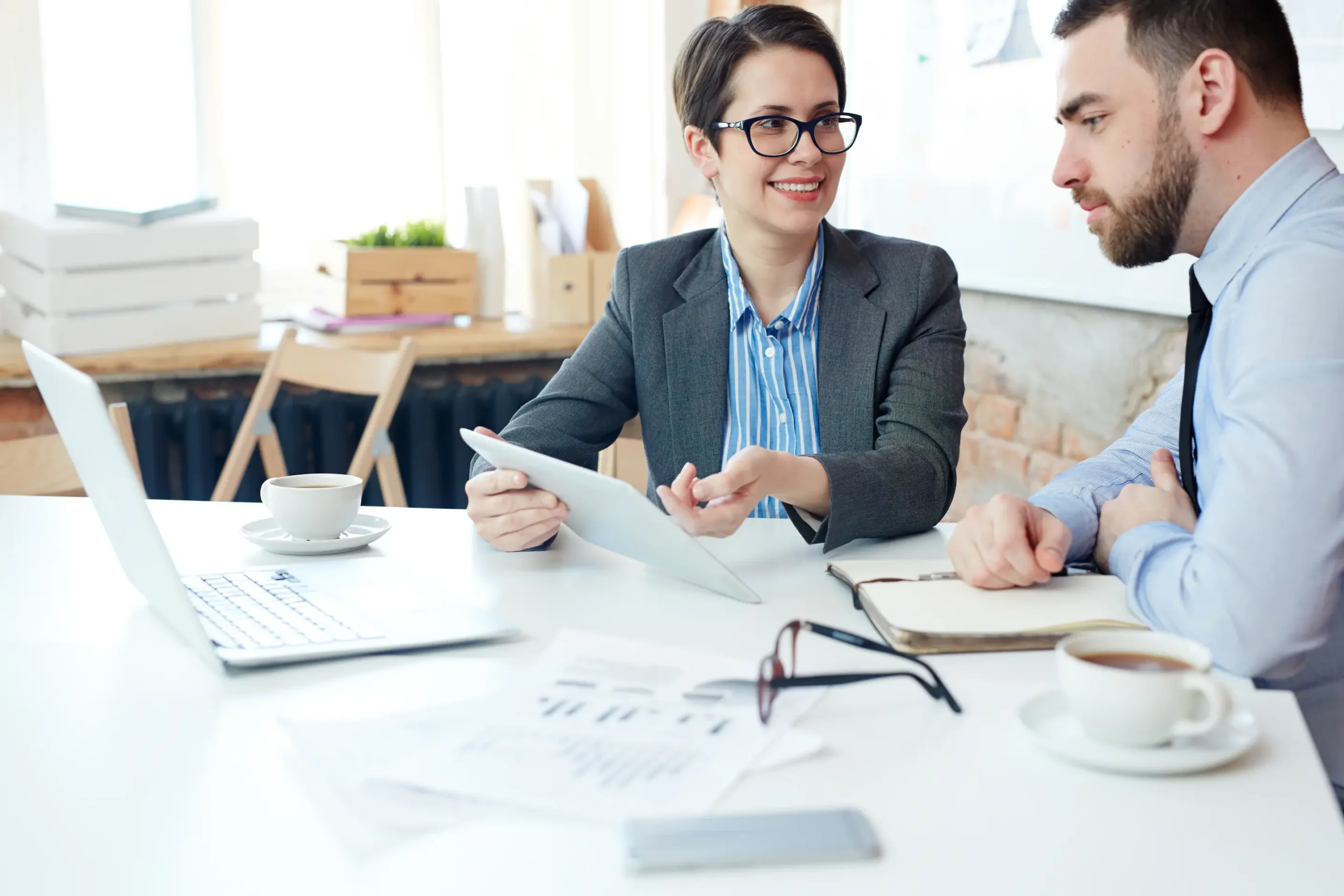 "Business professionals discussing financial strategy with tablet and laptop in modern office meeting"