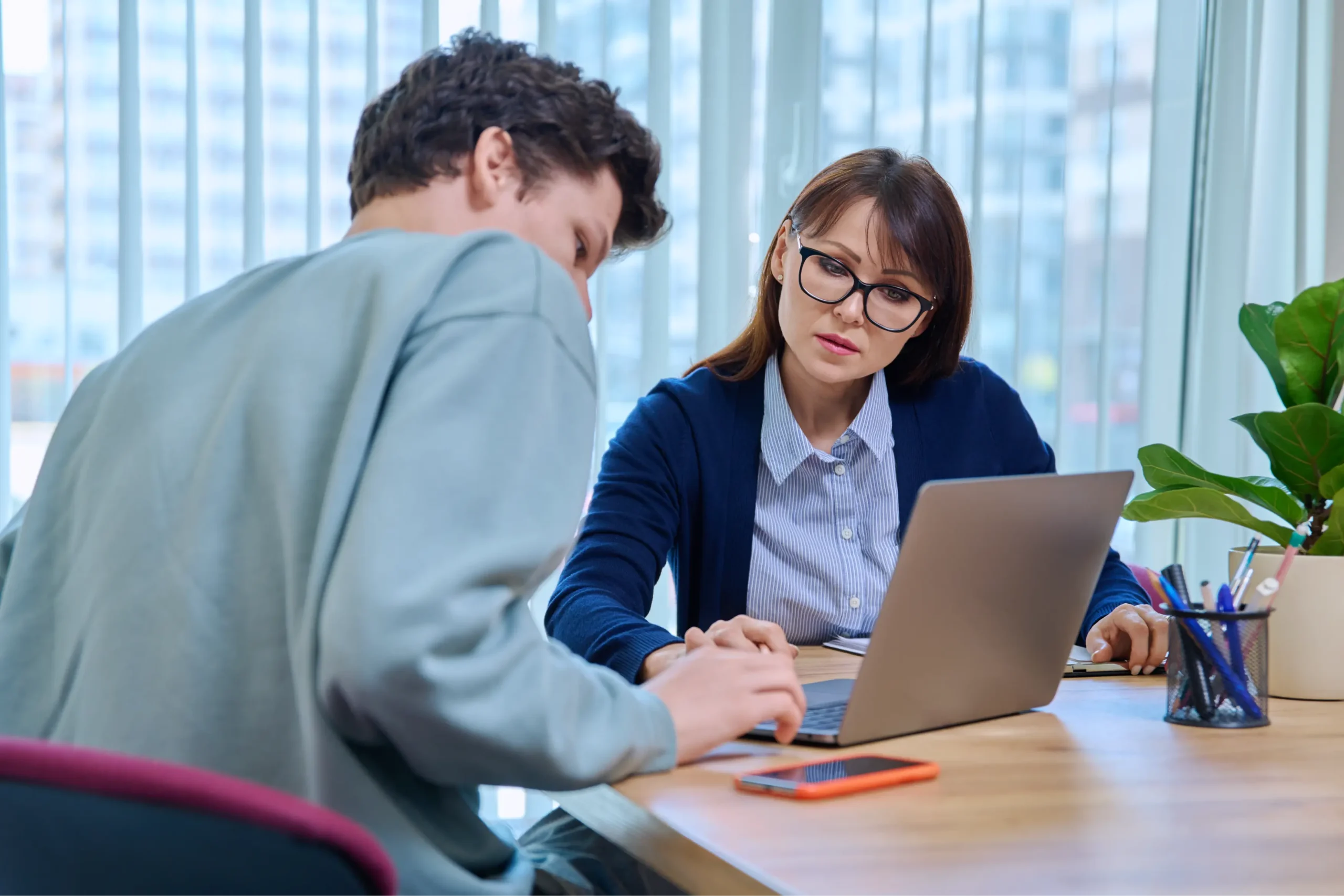 "Professional counselor meeting with student in modern office setting with laptop"