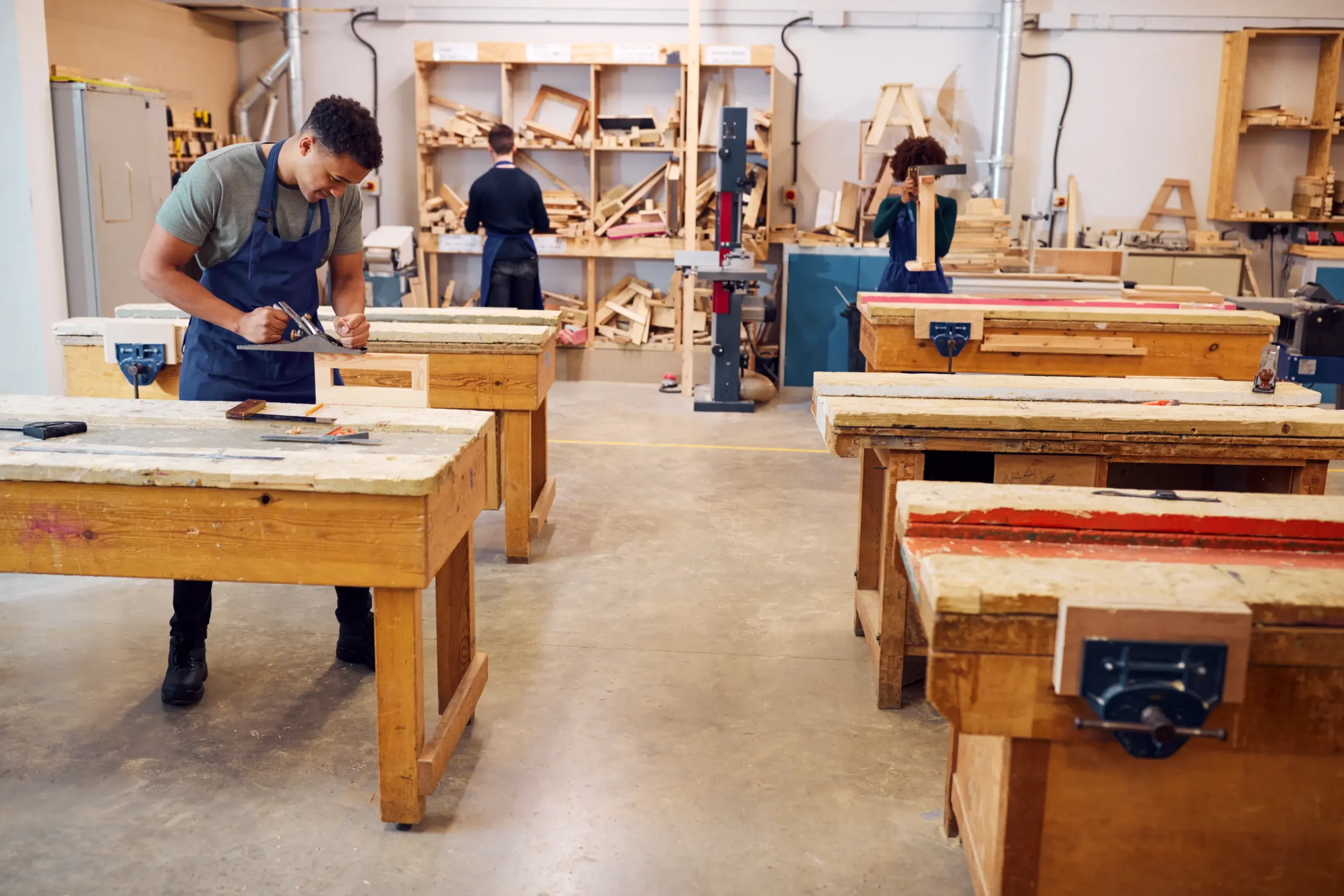 "Students working in carpentry workshop with wooden workbenches and tools during vocational training"