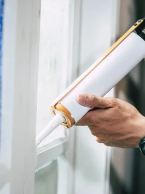 "Professional applying caulk sealant to window frame with caulking gun for weatherproofing"