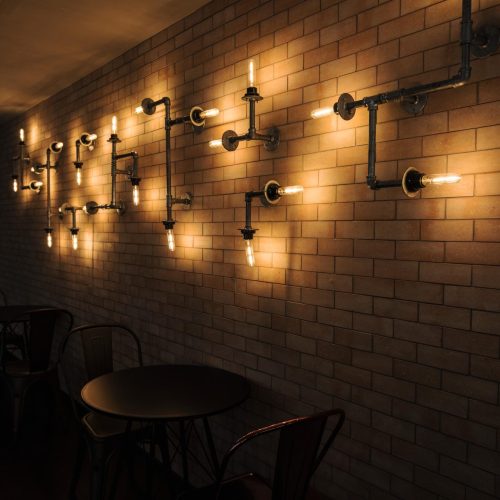 "Industrial-style cafe interior with exposed brick wall featuring vintage pipe wall sconces and metal chairs"