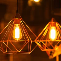 "Geometric diamond-shaped pendant lights with Edison bulbs in warm orange glow against dark background"