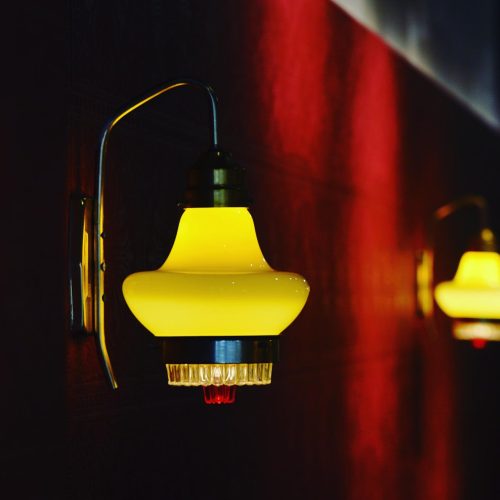 "Vintage yellow pendant lamp with curved arm mount against dark red wall"