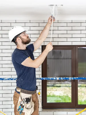 "Professional electrician installing ceiling light fixture during home renovation wearing safety helmet and work gear"