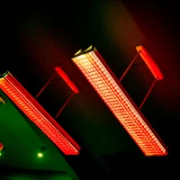 Red industrial fluorescent light fixtures mounted diagonally on dark ceiling with green ambient lighting